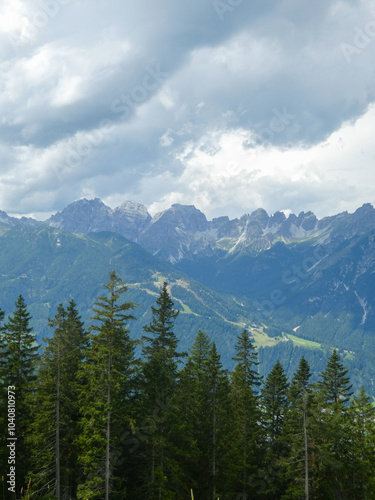 The Stubai Valley showcases the breathtaking peaks of the Austrian Alps under a dramatic sky. Tall pine trees frame the majestic view, highlighting the untouched beauty of the Tyrolean landscape