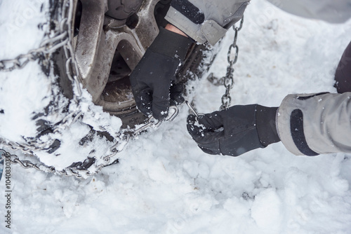 Travel in wintertime, close up view of the hands of an unrecognizable person putting chains on the wheels of an SUV vehicle, in order to be able to move forward over the snow on a mountain road.