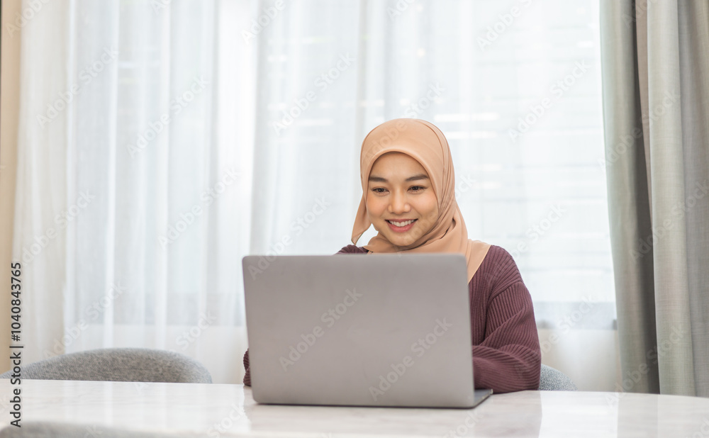 Muslim woman in hijab working on laptop sitting at desk in cozy home office, study on her task, freelance work, online education, remote work from home, modern muslim female business professional Muslim woman in hijab working on laptop sitting at desk in cozy home office, study on her task, freelance work, online education, remote work from home, modern muslim female business professional