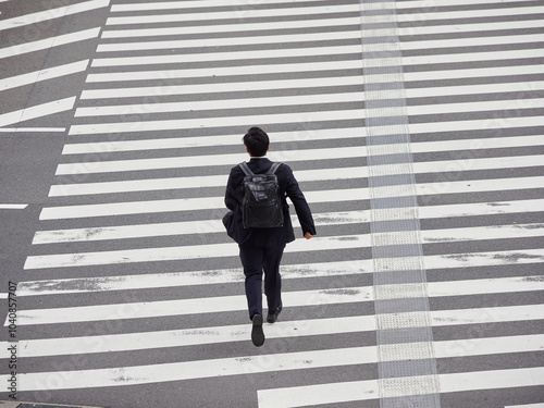 ローアングルで撮影した日本の都市の交差点の横断歩道を急いで渡る一人の若い男性営業マンの姿 photo