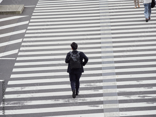 ローアングルで撮影した日本の都市の交差点の横断歩道を急いで渡る一人の若い男性営業マンの姿 photo