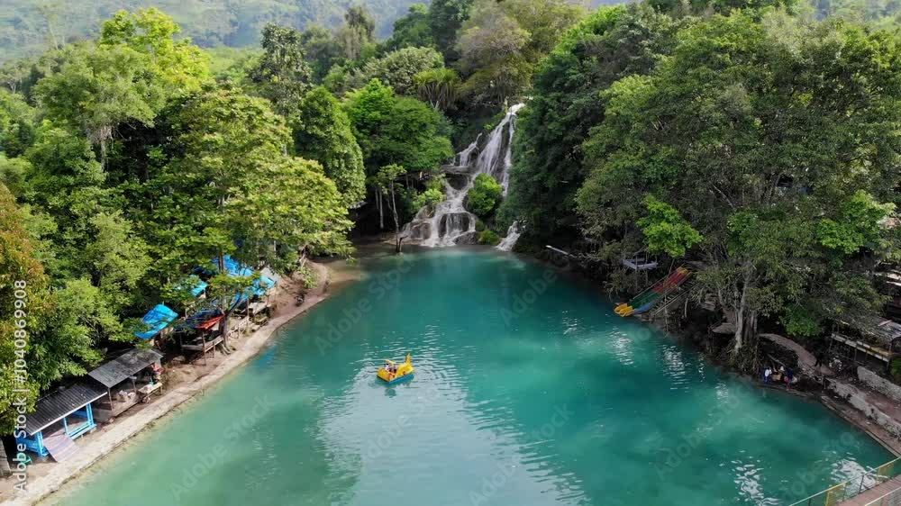 Aerial video of the beauty of a waterfall which has a pool of clear blue water surrounded by green trees