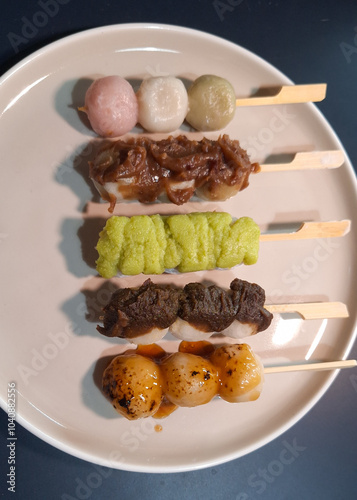 Top view of Mitarashi, Hanami, Houjicha, Zunda, and Yomogi anko dango on a white plate on navy table. Dango is a traditional sweet in Japan. photo