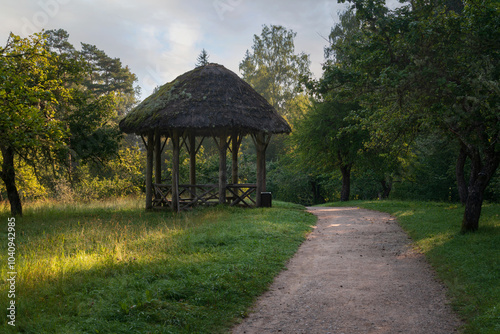 View of the ancient wooden gazebo in the apple orchard in the Mikhailovskoye Estate of the Pushkin Museum-Reserve on a sunny summer day, Pushkinskiye Gory, Pskov region, Russia photo