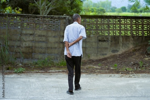 An old man walks across the street with his hands crossed behind his back.