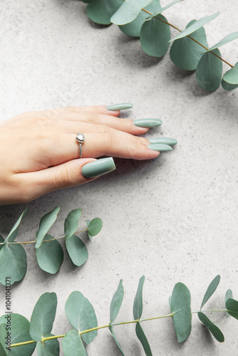 Elegant green nails showcased alongside fresh eucalyptus leaves on a soft gray surface