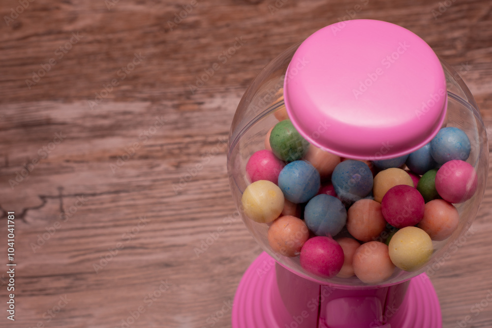 Obraz premium Pink gumball machine with a clear glass container full of colorful gumballs