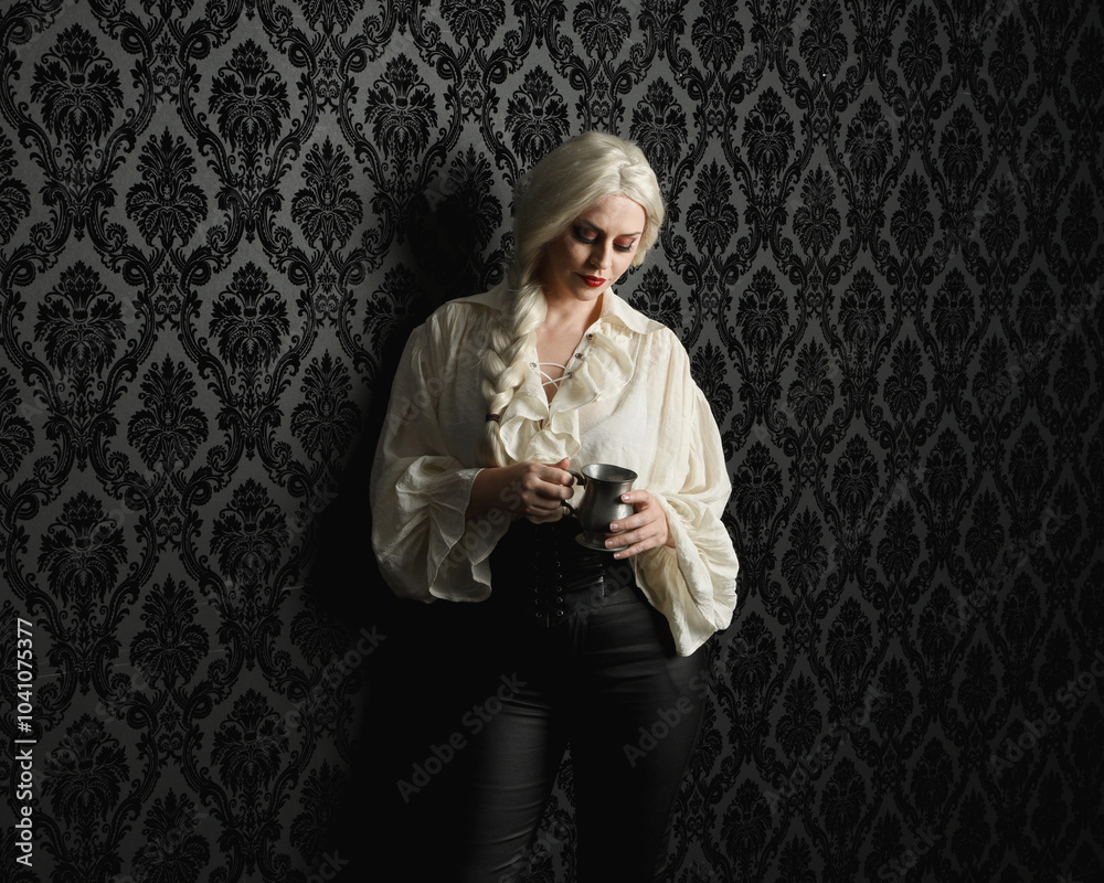 Fototapeta premium close up portrait of beautiful blonde female model, wearing vintage gothic fantasy ruffle blouse white shirt, leather pants, blonde hair holding wine drinking goblet. black brocade wallpaper backdrop