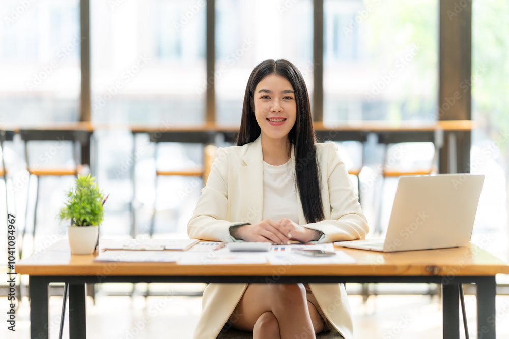 Confident Businesswoman at Desk: A professional woman in a white blazer sits at a desk with a laptop, exuding confidence and success. The image evokes a sense of ambition, focus, and determination.  