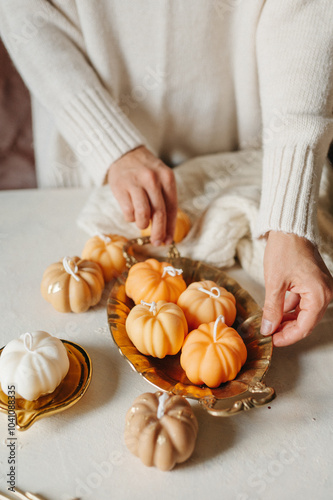 Handmade wax candle in the shape of pumpkins in the hands of a girl