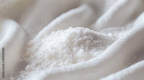 A close-up of a small pile of white powder, like baking soda, flour, or powdered sugar, on a white fabric background.