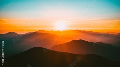 A fiery sunset over a vast mountain range with a warm glow illuminating the sky.