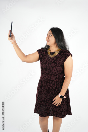 Portrait girl taking with social group using mobile phone on white background wall, wearing brown velvet dress, wrist watch.