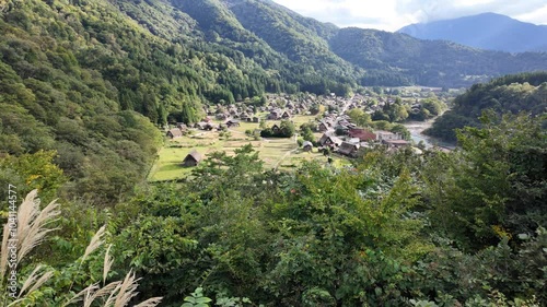 Shirakawa village, Gifu, Japan. A serene village nestled among lush mountains, surrounded by greenery and a clear sky, showcasing nature's beauty and tranquility.