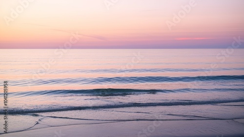 Calm ocean with soft waves under a pink and golden sunrise.