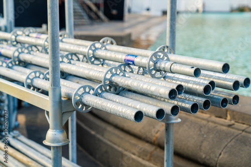 Wallpaper Mural Several galvanized metal scaffolding pipes are stacked and secured on a frame at a bustling construction site next to a serene waterfront. Torontodigital.ca