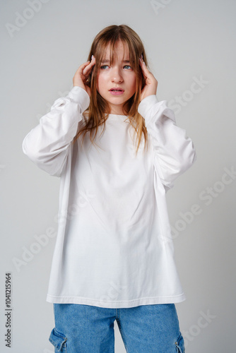 Young girl in a white sweater holding her head in discomfort against a minimalist background