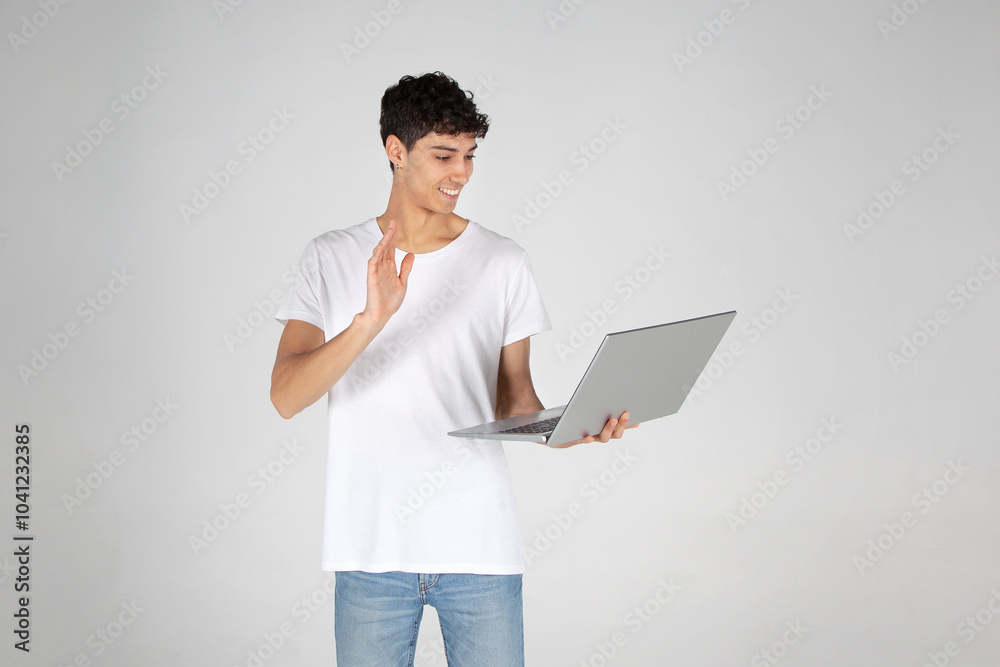 Joven con camiseta blanca y vaqueros, de pie, sosteniendo un portátil y mirando a cámara. Oferta Black Friday, venta online, publicidad. Joven con camiseta blanca y vaqueros, de pie, sosteniendo un portátil y mirando a cámara. Oferta Black Friday, venta online, publicidad.