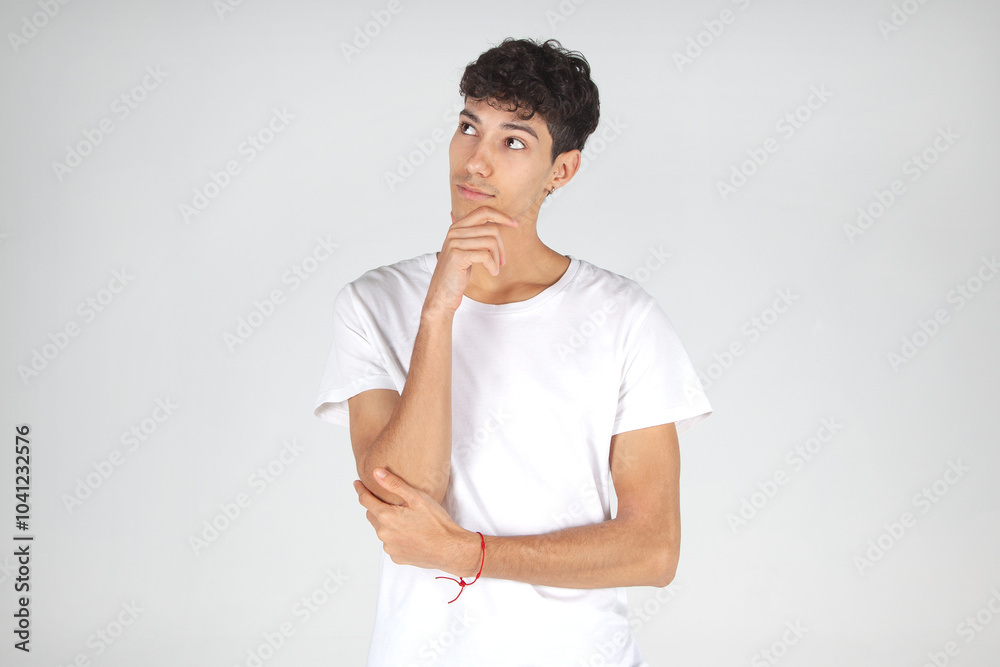 Chico joven caucásico pensando, con camiseta blanca y jeans, mano en la boca, mirando hacia un lado. Anuncio publicitario para campañas online. Chico joven caucásico pensando, con camiseta blanca y jeans, mano en la boca, mirando hacia un lado. Anuncio publicitario para campañas online.