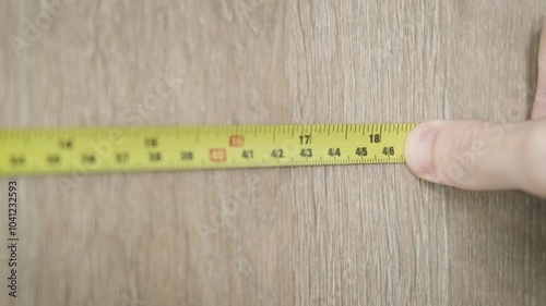 Close-up of a hand holding a yellow measuring tape against a textured wooden surface, focusing on precision and detail in a carpentry or home improvement project. Ideal for construction or DIY tasks. photo