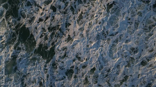 Top-down drone view of ocean waves at sunset, capturing the beautiful motion of the water and the warm evening light.