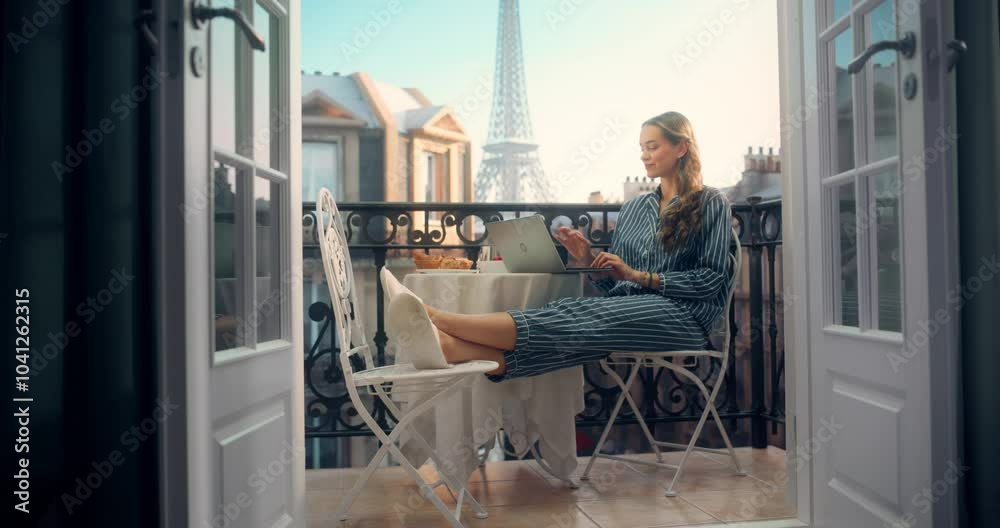Woman in Pajamas Enjoying a Quiet Breakfast with Coffee while Using Her Laptop on a Balcony. She Casually Put Her Feet on a Chair and Shops Online as the Eiffel Tower Stands Tall in the Distance
