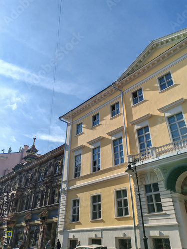 A three-story building with a pale yellow exterior and symmetrical windows, featuring a prominent arched entrance. The classical design evokes a sense of history and grandeur in urban architecture.