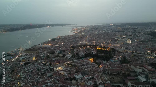 Drone panorama of evening Lisbon, capturing the cityscape illuminated by warm lights, with iconic landmarks and the scenic urban landscape.