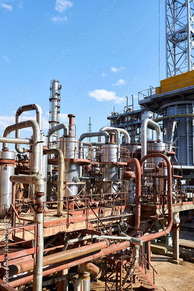 Old distillation column towers and reactors under blue evening sky background at chemical plant. Exterior of silver metal rusty enterprise with copyspace.