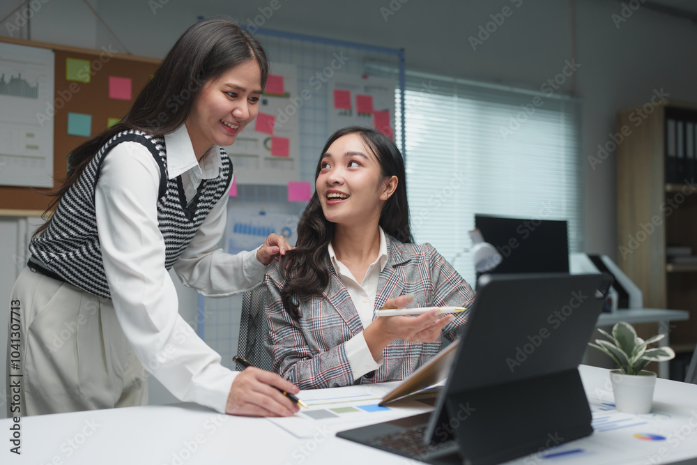 Two young businesswomen discuss the details of their planning, operations, and income during coffee breaks at their desks happily. Two young businesswomen discuss the details of their planning, operations, and income during coffee breaks at their desks happily.