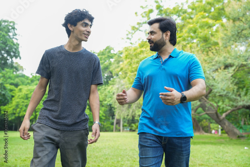 indian father and son talking while walking in a public summer park or garden. bonding, parenthood concept.