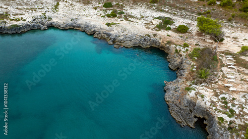 Aerial view of a cliff and the blue sea. There are two people swimming in the bay.