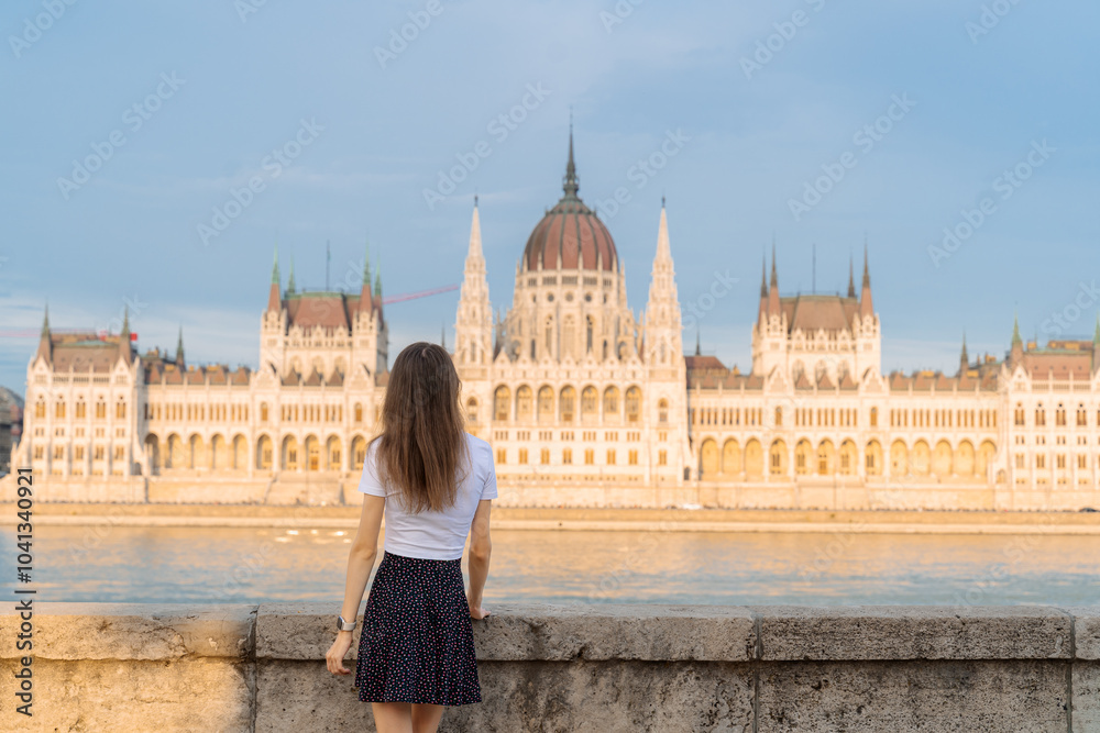 Fototapeta premium Tourism in Europe. Back view of young woman enjoying view of Hungarian Parliament Building on Danube River in Budapest, Hungary.