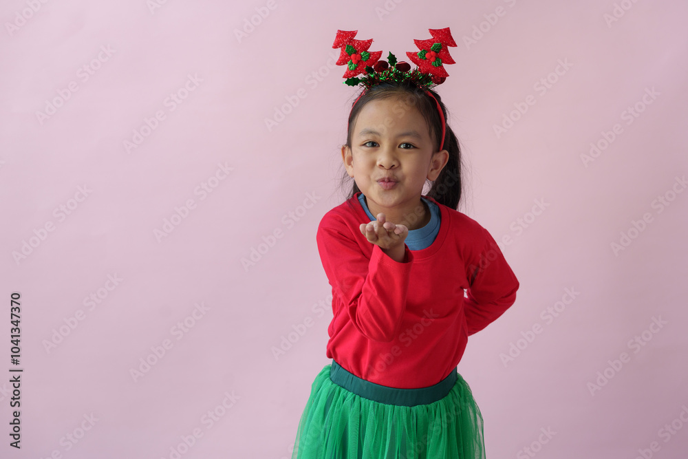 Adorable little Asian girl with Christmas tree headband, antlers showing various poses, standing, smiling, laughing, having fun in various poses, pink background. Holiday concept annual festival. Adorable little Asian girl with Christmas tree headband, antlers showing various poses, standing, smiling, laughing, having fun in various poses, pink background. Holiday concept annual festival.