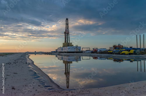 Drilling oil and gas wells in desert terrain. Sand hills, sparse vegetation. Beautiful sky. Infrastructure of the drilling rig