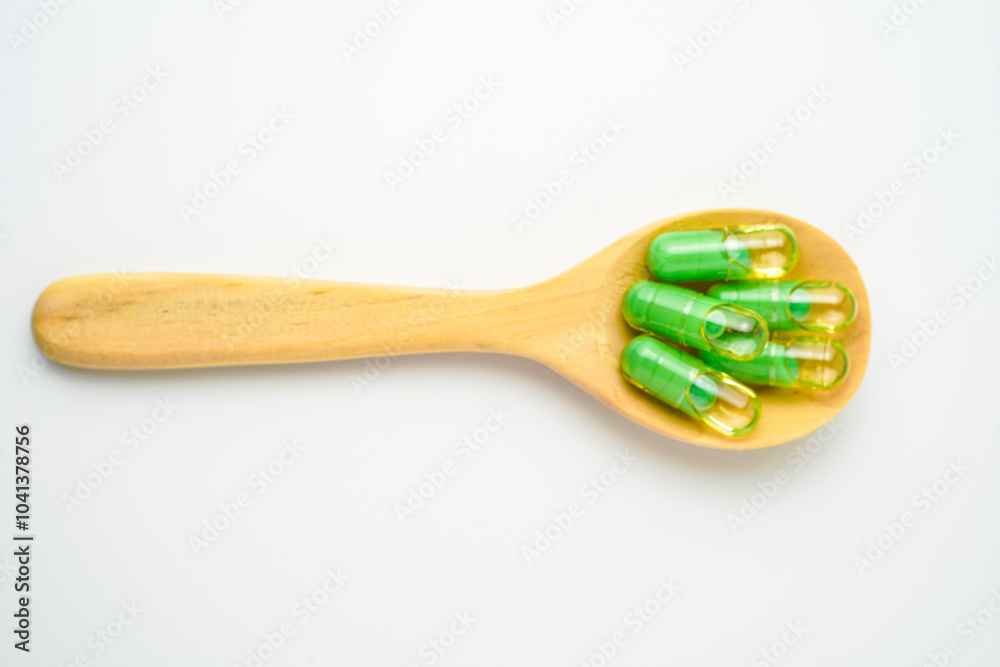 transparent capsules pills with a mixture of green powder and oil in wooden spoon, vitamin supplements transparent capsules pills with a mixture of green powder and oil in wooden spoon, vitamin supplements