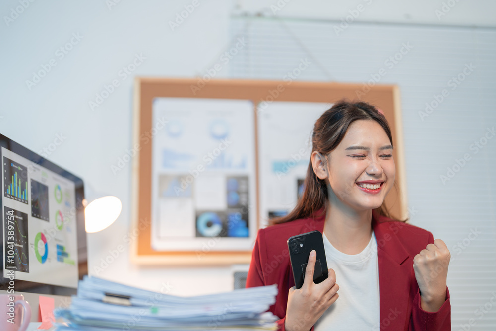 Young businesswoman is working in a modern office, she is very happy and excited about the good news she received on her smartphone Young businesswoman is working in a modern office, she is very happy and excited about the good news she received on her smartphone