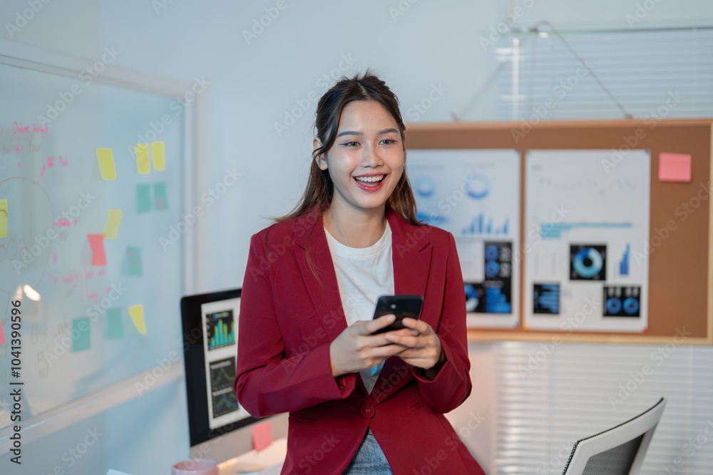 Confident young manager in modern office, smiling and using smartphone for business communication. Walls display charts symbolizing career success Confident young manager in modern office, smiling and using smartphone for business communication. Walls display charts symbolizing career success