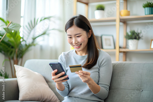 Happy asian woman buying electronic services application using card and smartphone sitting sofa at home.png