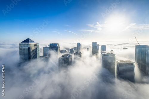 Fototapeta Naklejka Na Ścianę i Meble -  The modern skyline of London, Camary Wharf disctrict, during an autumn day with fog and the tops of the skyscrapers looking out above the clouds
