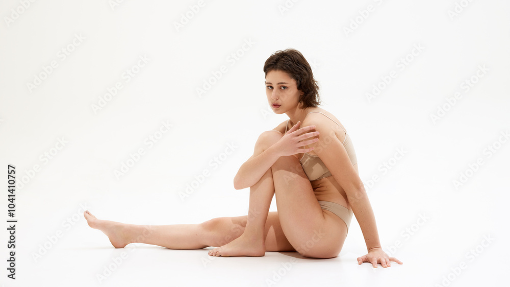 Portrait of young woman sitting on floor in neutral lingerie, embodies balance between health, beauty against white studio background. Concept of spa procedure, self-care treatments, self-love. Ad Portrait of young woman sitting on floor in neutral lingerie, embodies balance between health, beauty against white studio background. Concept of spa procedure, self-care treatments, self-love. Ad