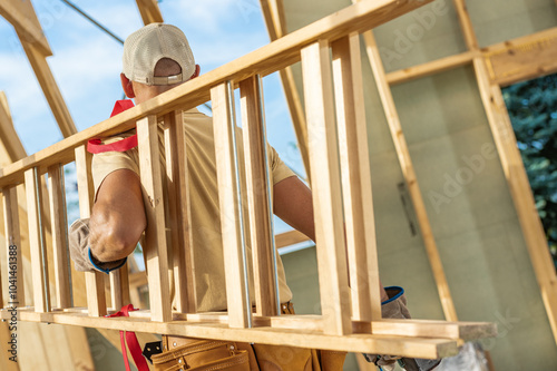 Carpenter Lifts Wooden Structure at a Construction Site Under a Clear Blue Sky photo