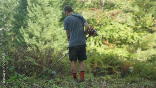 Landscaper using weed whacker on ferns and vegetation (Slow Motion 4k 30p) photo