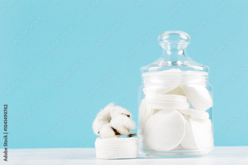 Cotton pads in glass jar and flower on blue background