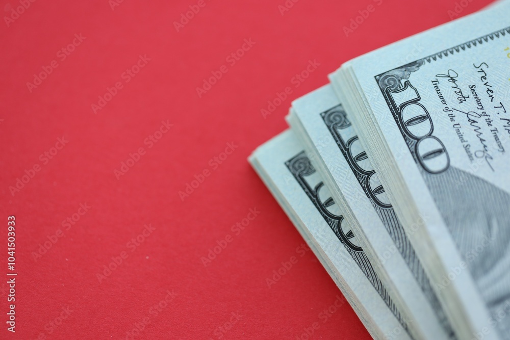 Big amount of hundred dollar bills in thick stack lies on bright red color paper background Big amount of hundred dollar bills in thick stack lies on bright red color paper background