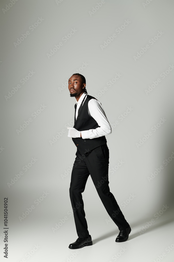 A young African American man stands poised in a tailored suit, showcasing elegance and style with a grey background. A young African American man stands poised in a tailored suit, showcasing elegance and style with a grey background.