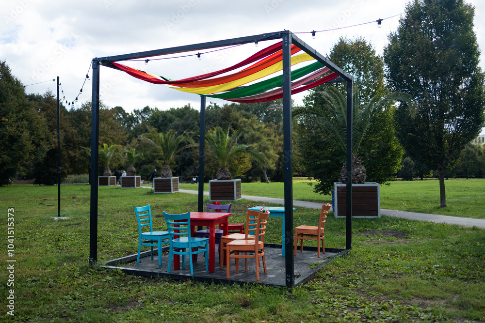 Beautiful modern gazebo with observation chairs and a table for relaxing in a city summer park Beautiful modern gazebo with observation chairs and a table for relaxing in a city summer park
