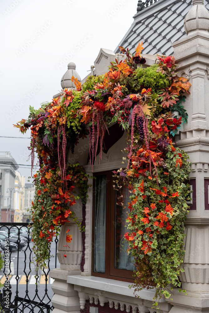 Side view of orange fall garland decoration made from small artificial pumpkins and maple leaves around window of autumn festival kiosk building. Soft focus. City street festive decor theme. Side view of orange fall garland decoration made from small artificial pumpkins and maple leaves around window of autumn festival kiosk building. Soft focus. City street festive decor theme.