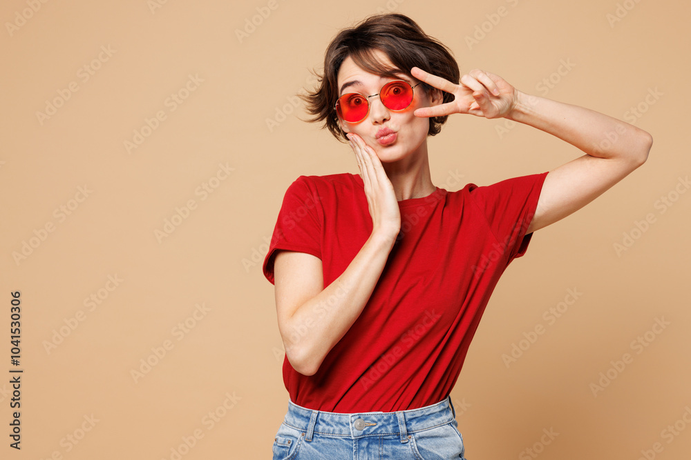 © ViDi Studio - Young smiling happy fun woman she wear red t-shirt casual clothes sunglasses cover eye with victory sign look camera isolated on plain pastel light beige background studio portrait. Lifestyle concept.