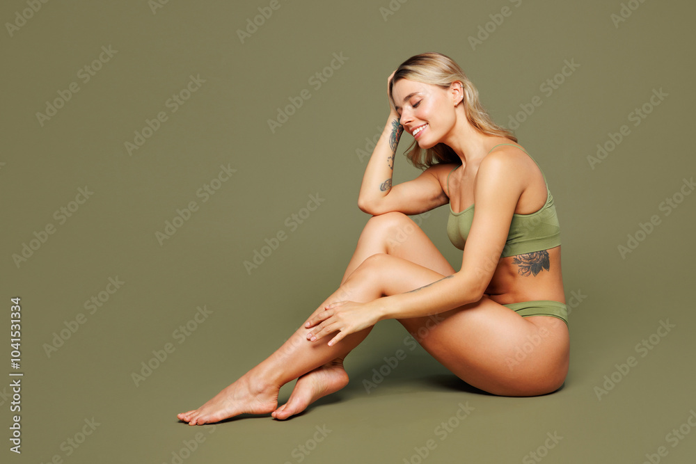 Naklejka premium Full body side profile view young smiling happy satisfied nice lady woman with slim skinny body perfect skin wear top bra lingerie sits isolated on plain green background. Lifestyle diet fit concept.